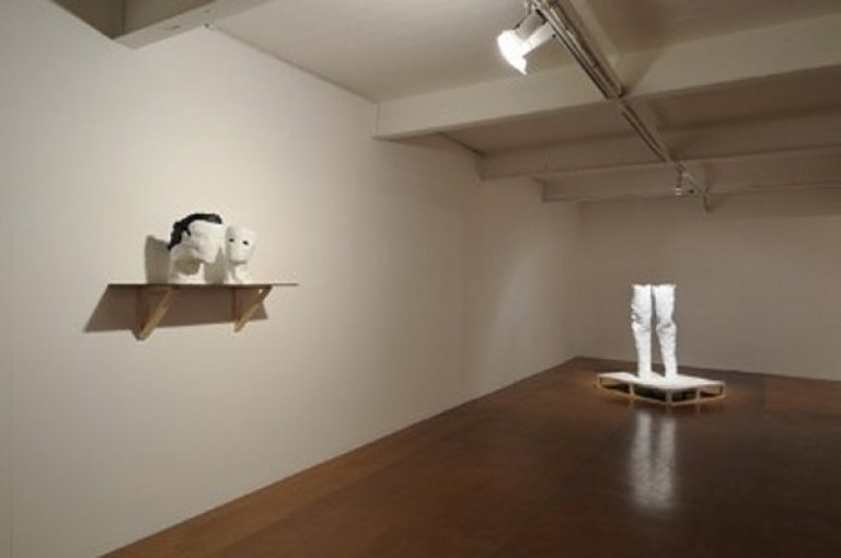 Lit up sculptures of heads on a shelf on the wall and a sculpture of legs standing on the floor